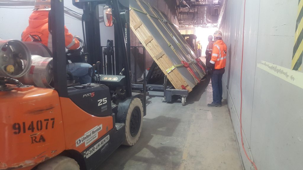 Two forklifts are rigged on both sides of the heavy cart to transport it down the narrow hallway.